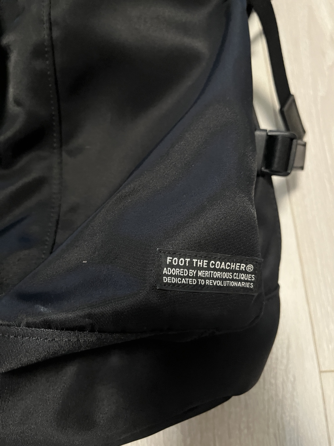 所有バックパックのFOOT THE COACHERブランドタグと、黒いナイロン生地の接写。